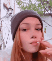 a girl wearing a beanie smoking a cigarette