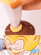 a close up of a person frosting a cupcake with a picture of sonic the hedgehog in the background