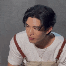 a young man wearing a white shirt and suspenders looks at the camera