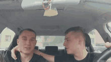 two men are sitting in a car and one of them is holding the other 's neck .