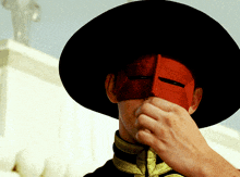 a man wearing a black hat and a red mask covers his face
