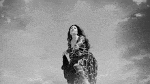 a woman in a dress is standing in front of a cloudy sky in a black and white photo .
