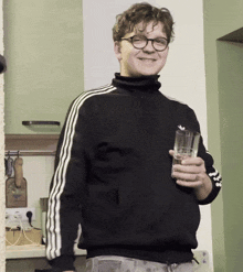 a young man wearing glasses and a black adidas sweater holds a glass of beer