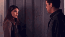 a man and a woman are standing next to each other in front of a door and looking at each other .