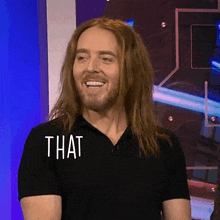 a man with long hair and a beard is smiling with the word that on his shirt