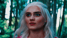 a close up of a woman 's face in a forest with trees in the background