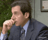 a man in a suit and tie is sitting at a table with his hand on his mouth .
