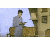 a man in a suit is holding a gun in a living room with a couch and lamp