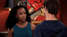a man and a woman looking at each other with a painting in the background