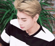 a young man with blonde hair is wearing a black and white striped t-shirt .