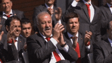 a group of men in suits and ties are clapping and smiling