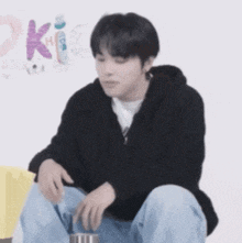 a young man in a black hoodie is sitting on the floor holding a cup .