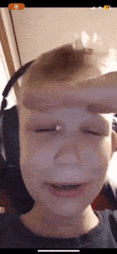 a young boy wearing headphones is holding a condom to his forehead .