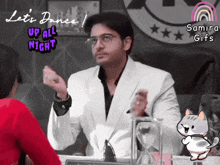 a man in a white suit is sitting in front of a sign that says let 's dance