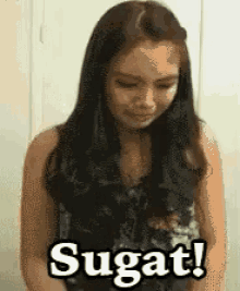a woman is standing in front of a sign that says ' sugat ! ' on it .