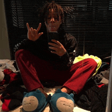 a man is sitting on the floor wearing a pair of slippers and taking a selfie with his cell phone .