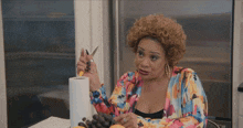 a woman sitting at a table cutting a roll of paper towels with a pair of scissors