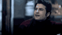 a man wearing a black turtleneck and a red jacket is looking at the camera