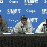 a man is sitting at a table with microphones in front of a blue wall that says playoffs