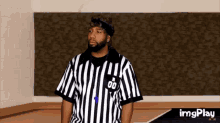 a referee wearing a striped shirt with the number 00 on it is standing in a room .