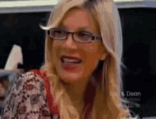 a woman wearing glasses and a floral shirt smiles