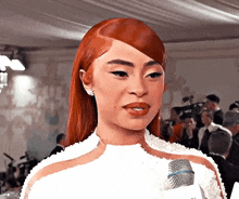 a woman with red hair is wearing a white dress and talking into a microphone