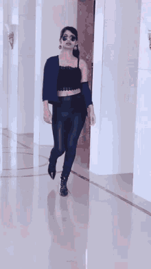 a woman in a black crop top and blue pants is walking down a hallway