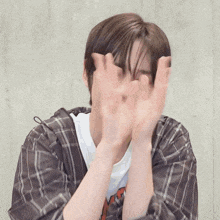 a young man in a plaid shirt covering his face