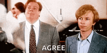 two men in suits and ties are standing next to each other and shaking hands . one of the men is saying `` agree '' .