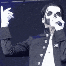 a man with a skull painted on his face is holding a microphone .