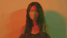 a woman with long hair stands in front of an orange wall