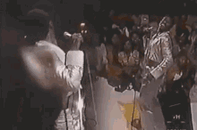 a man in a suit is singing into a microphone in front of a crowd .