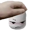 a person is holding a marshmallow with a sad face on it .