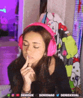 a woman wearing pink headphones is sitting in a chair with her eyes closed and her finger on her chin .