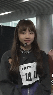 a girl wearing a microphone and a fifty fifty shirt is standing in a room .