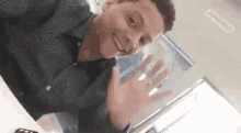 a young man is smiling and waving at the camera while sitting at a desk .
