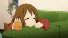 a girl laying on a green couch holding an orange in her hand