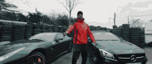 a man in a red jacket stands in front of a stack of tires