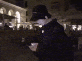 a man in a black hat stands in front of a crowd of people in a dark street
