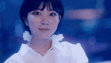 a woman wearing a white shirt and white earrings looks at the camera .