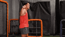 a man in a red tank top is standing in front of a cage