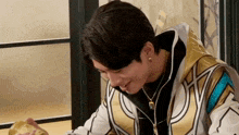a man in a gold and white jacket is sitting at a table with a glass of beer in his hand .