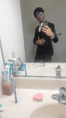 a man taking a selfie in front of a mirror with a pack of crest toothpaste on the counter