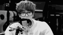 a black and white photo of a young man wearing glasses and headphones talking into a microphone .
