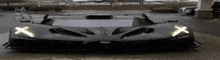 a black sports car is parked in a parking lot with the headlights on .