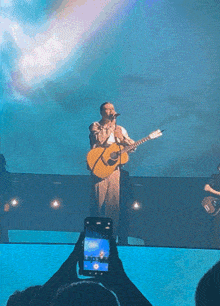 a man singing into a microphone while holding a guitar on stage