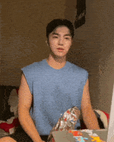 a man in a blue tank top sits in front of a laptop with the word mission on the wall behind him