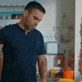 a man in a blue shirt is standing in a kitchen looking down .