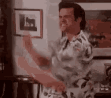 a man in a hawaiian shirt is dancing in a living room with a picture on the wall behind him .