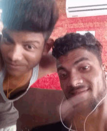 two men are posing for a picture and one of them is wearing ear buds